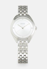 Montre en acier inoxydable argenté avec un boîtier rond, un cadran blanc, trois aiguilles et des accents en cristal. Elle est dotée d'un bracelet à maillons poli.