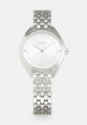 Montre en acier inoxydable argenté avec un boîtier rond, un cadran blanc, trois aiguilles et des accents en cristal. Elle est dotée d'un bracelet à maillons poli.