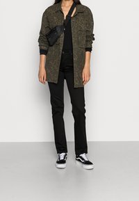 Camisa de overshirt con estampado de olivas, top negro, jeans negros y zapatillas negras con detalles en blanco. Bandolera negra con detalle de cremallera.
