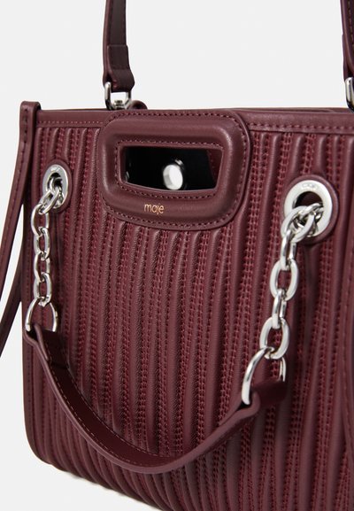 Bordeaux leren handtas met verticale ribbelstructuur, zilveren kettingaccenten en een bovenhandgreep. Beschikt over een uitsnijding in de handgreep en een logo.