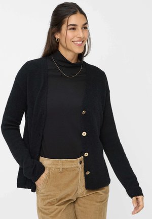 Cardigan nero a maglia con maniche lunghe e una consistenza morbida. Caratterizzato da bottoni dorati e una vestibilità rilassata, abbinato a un dolcevita nero.