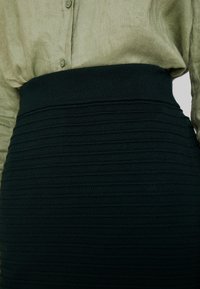 Mörkgrön rippad stickad kjol med ett brett elastiskt midjeband, i kombination med en ljusgr ön, knappad, texturerad skjorta.