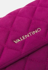 Borsa a tracolla in suede viola trapuntato con logo dorato "Valentino". Texture liscia con un motivo a diamante e design a pattina piegata.