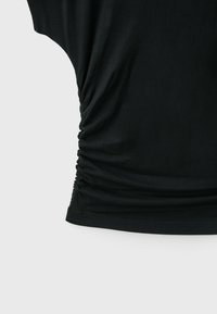 Tissu noir avec des détails froncés rassemblés le long de la couture latérale et un ourlet simple en bas.