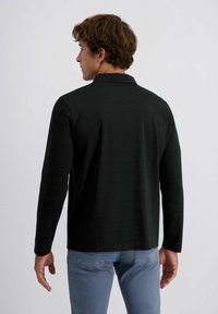 Schwarzes Langarmshirt mit feinem gestreiften Textur, Kragen, und geradem Saum, kombiniert mit hellblauen Jeans.