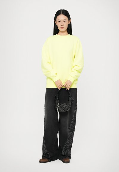 Neon gul oversized sweatshirt, sorte vide bukser med teksturerede side mønstre, og en lille sort perle-handtaske.