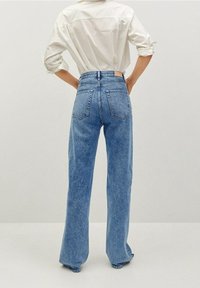 Jeans de tiro alto en azul claro con diseño acampanado, que cuentan con bolsillos traseros y una textura desgastada. Combinados con una camisa blanca de botones.