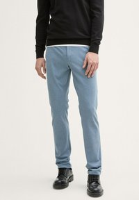 Lichtblauwe tapered broek van zachte stof, met een gladde textuur en zijzakken. Gecombineerd met zwarte veterschoenen.