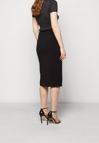Jupe crayon noire jusqu'aux genoux avec un design ajusté, associée à des sandales à talons hauts noires. Le haut présente un tissu texturé et brillant.