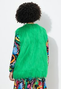 Faux fur-väst i knallgrön med långa, texturerade fibrer. Mönstrad långärmad klänning med livfulla färger och abstrakta mönster.