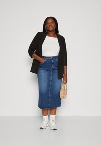 Black blazer over a white top, paired with a blue denim midi skirt, white socks, and chunky sneakers. Holding a beige handbag.