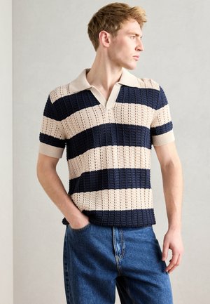 Strikket polo-skjorte med v-hals, i marineblå og kremfargede horisontale striper, kort erme og en teksturert mønster. Kombinert med blå jeans.