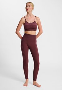 Bordeaux activewear set, inclusief een geribd crop top met dunne bandjes en high-waisted legging met contrasterende roze stiksels.