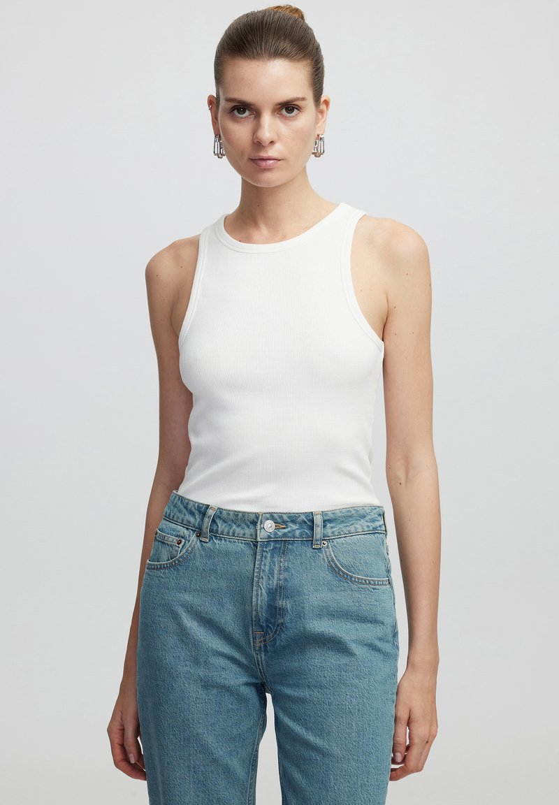 Top de tirantes blanco con canalé y cuello redondo, combinado con jeans de tiro alto en azul claro, que cuentan con un cierre de botón y bolsillos laterales.