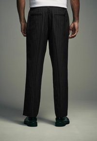 Black pinstriped trousers with a straight cut, featuring two back pockets and worn with black shoes. The fabric has a smooth texture.