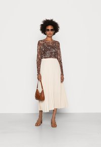Top longo transparente castanho com padrão de leopardo, saia midi plissada branca, mala castanha e sandálias de salto bloco.