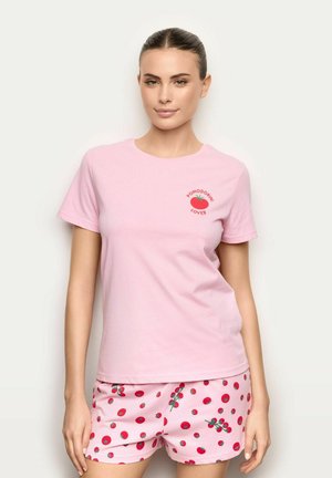 Femme portant un t-shirt rose clair avec un motif de tomate rouge et le texte « Pomodorini Lover », associé à un short rose assorti couvert de motifs de tomate.
