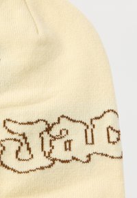 Πλεκτός σκούφος σε ανοιχτό κρέμ χρώμα με καφέ γράμματα. Μαλακή υφή, εφαρμοστή εφαρμογή, διαθέτει στρογγυλή κορυφή και διπλωμένο γείσο με σχέδιο με έντονα γράμματα.