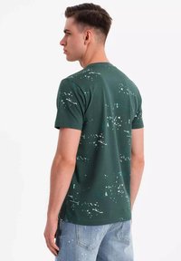 Grøn bomulds T-shirt med rund hals, der har et sprøjtet maleri-design i hvidt og lysblåt på ryggen. Korte ærmer og afslappet pasform.