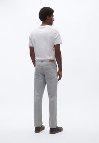 Sivé rifľové nohavice s voľným strihom, piatimi vreckami a svetlohnedou nášivkou na opasku, kombinované s bielym jednofarebným tričkom a modrými topánkami.