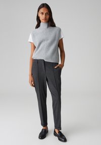 Top senza maniche a coste grigio sopra una camicia bianca, abbinato a pantaloni tailored grigio scuro e mocassini neri. Design minimalista e vestibilità snella.