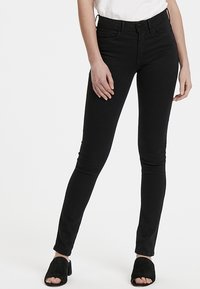 Černé skinny džíny z denimu s klasickým designem pěti kapes, s knoflíkovým zapínáním a poutky na pásek. Hladká textura, tapered střih.