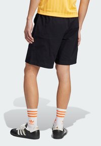 Black shorts with a textured fabric, paired with white socks featuring orange stripes and black athletic shoes with white and gold accents.
