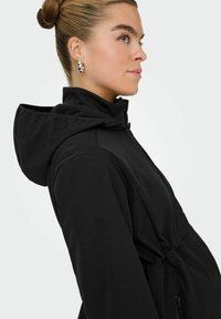 Černá kapucňová bunda s přiléhavým střihem, má zúžený pas a zipové kapsy, vyrobená z hladkého, měkkého materiálu.