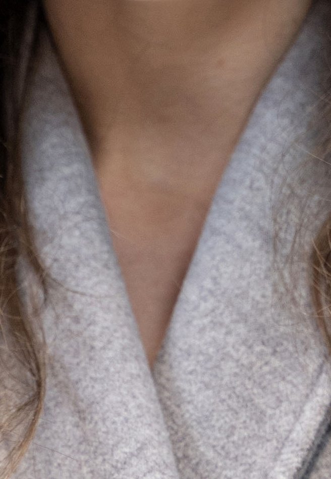 Gros plan d'une personne portant un manteau gris clair texturé avec de longs cheveux bruns visibles sur les côtés.