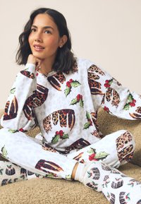 Pyjamaset met patroon van feestelijke taarten en hulstontwerpen in wit, met accenten van luipaardprint. Gemaakt van zachte, gestructureerde stof.