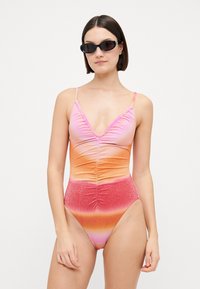 Maillot de bain une pièce en dégradé de rose, orange et rouge ; tissu doux avec des détails froncés ; décolleté en V plongeant et bretelles ajustables ; finition scintillante.