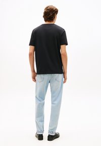 Μαύρο βαμβακερό μπλουζάκι με κοντά μανίκια, σε συνδυασμό με ανοιχτόχρωμο μπλε τζιν παντελόνι. Το μοντέλο φορά μαύρα παπούτσια, ορατά από πίσω.