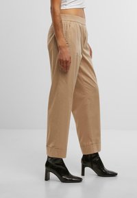 Pantaloni beige, sartoriali, con una vestibilità rilassata, vita elasticizzata e orli arrotolati, abbinati a stivali neri alla caviglia. Tessuto dalla texture liscia.
