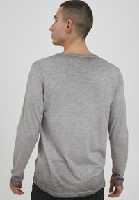 Langærmet grå skjorte med tekstureret, meleret stof, der har en rund halsudskæring og en subtil gradient fra lys til mørkere grå ved kanten.