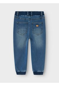 Pantalones jogger de mezclilla azul con una cintura acanalada, que presentan dos bolsillos traseros y una pequeña etiqueta de marca. Textura suave, tobillos ajustados.