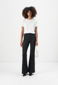 White short-sleeve t-shirt paired with high-waisted black flared pants. Model holds a small pink handbag. Simple, clean design.