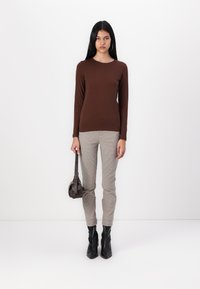 Top maro cu mânecă lungă, combinat cu pantaloni ajustați în carouri; ghete negre până la gleznă; ținând o geantă mică de culoare închisă. Textură netedă, design simplu.