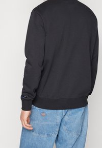 Sudadera negra con cuello redondo, puños y dobladillo acanalados, hecha de un tejido suave; combinada con pantalones de mezclilla azul claro que cuentan con bolsillos.