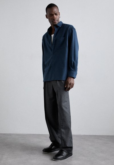Mörkblå knäppt skjorta med bröstficka, kombinerad med grå vida byxor och svarta skor, med slät textur och avslappnad passform.