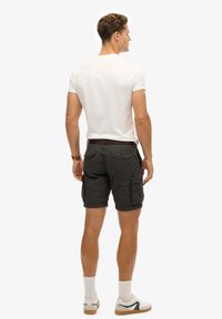 Grijze cargoshorts met meerdere zakken, gecombineerd met een effen wit t-shirt. De shorts hebben een gestructureerde stof en een bruine riem.