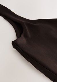Close-up of a dark brown sleeveless garment with a smooth, slightly shiny fabric and a thick strap on a light background.