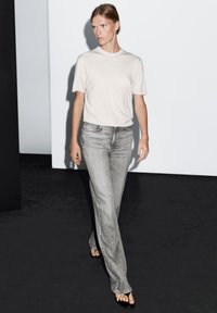 Light gray t-shirt paired with light gray straight-leg jeans. The outfit has a relaxed fit, with minimal stitching and flat sandals.