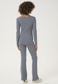 Prugasta majica s dugim rukavima i rastegnutih hlača u mornarsko plavoj i bijeloj boji, izrađena od mekanog, rastezljivog materijala. Karakteristike uključuju čamac izrez i uski kroj.