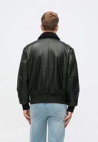 Must be black leatherist bomber jakk, millel on tekstuuriga sünteetilisest karvast kaelus. Varustatud soonikkrae ja hemiga, lõige on mugav. Kandmine helesiniste teksade kohal.