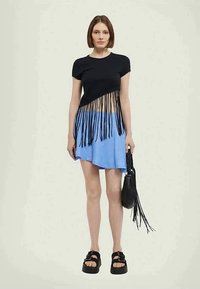 Tricou scurt negru cu margine franjurată, asortat cu o fustă asimetrică bleu deschis. Geantă neagră cu bandulieră și sandale negre cu talpă groasă.
