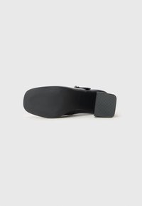 Black high-heeled shoe bottom with textured rubber sole, block heel, and no visible branding. Rounded toe and sleek design.