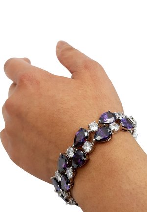 Gemme viola e trasparenti si alternano in un design di bracciale a catena, impostato in metallo tono argento, indossato su un polso abbronzato.