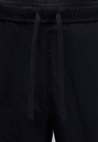 Črne športne kratke hlače s širokim elastičnim pasom z nastavljivimi vrvicami za zatezanje in subtilnimi zaključki šivov. Gladek tekstura tkanine.