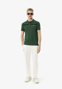 Grön randig piké med en marinblå stripe, kombinerad med vita byxor och ljusa sneakers, med en logotyp på bröstet.