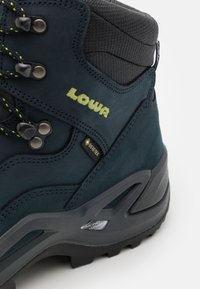 Mörkblå vandringskänga med strukturerad mocka, gröna detaljer, metallöglor och en robust sula med MONOWRAP-design.